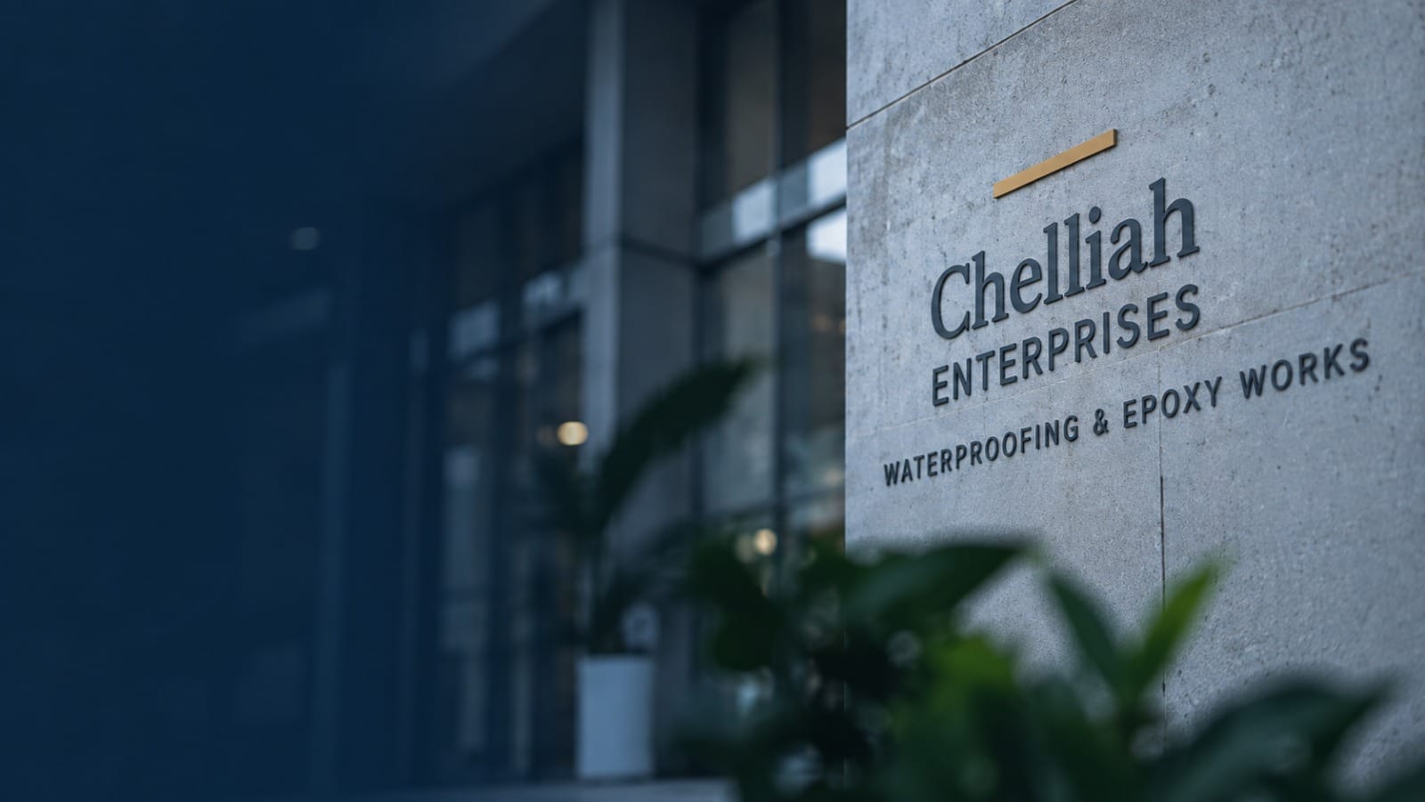 A concrete signage wall at a building entrance carrying the Chelliah Enterprises name and the line Waterproofing & Epoxy Works, with glazing and planting beyond it.