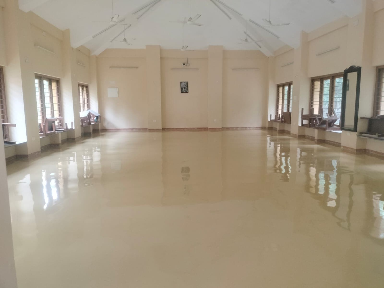 A finished hall with a glossy beige epoxy floor reflecting the ceiling fans and windows.